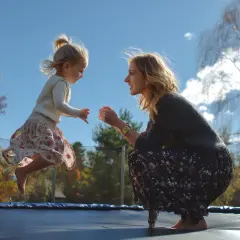 Matka i dziecko skaczą na trampolinie w słoneczny dzień.