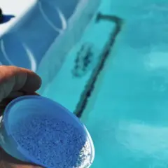 Dłoń wsypuje granulki bromu do błękitnej wody jacuzzi, dbając o czystość.