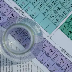 Okrugli predmet, poput čaše, leži na periodnom sustavu elemenata. Vidljivi su elementi poput Pu, Am, Cm, a u pozadini se nazire i 1 mol.