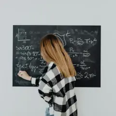 Dziewczyna w kratkę pisze wzór na tablicy. Wzór na t to skomplikowane równanie matematyczne.