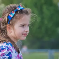 Uśmiechnięta dziewczynka z kokardką na głowie, jakby zastanawiała się, czy to maji czy mai.