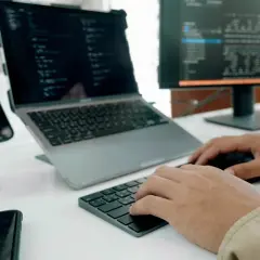 Programista pracuje nad nowym oprogramowaniem użytkowym, pisząc kod na laptopie i monitorze.