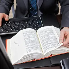 Mężczyzna w garniturze przegląda grubą księgę prawniczą, obok klawiatura.