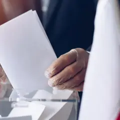 Ręka w rękawiczce wrzuca kartę do urny. Wybory, metoda Donty.