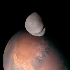 Niewielki, nieregularny księżyc Deimos unosi się nad czerwoną planetą Mars.