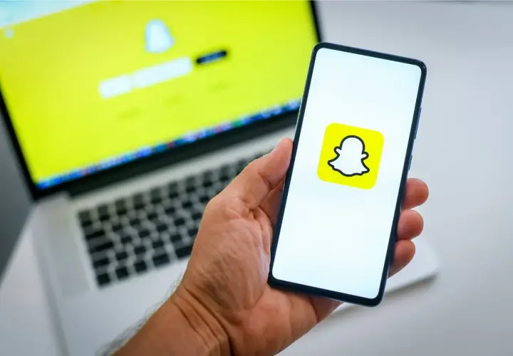 Chcesz wiedzieć, jak usunąć konto na Snapie? Na ekranie telefonu widać logo Snapchata, a na laptopie ekran logowania.