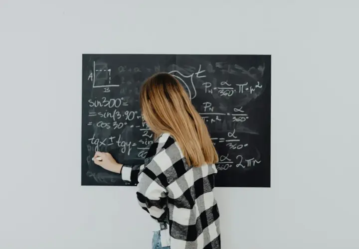 Dziewczyna w kratkę pisze wzór na tablicy. Wzór na t to skomplikowane równanie matematyczne.