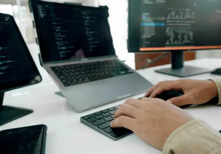 Programista pracuje nad nowym oprogramowaniem użytkowym, pisząc kod na laptopie i monitorze.