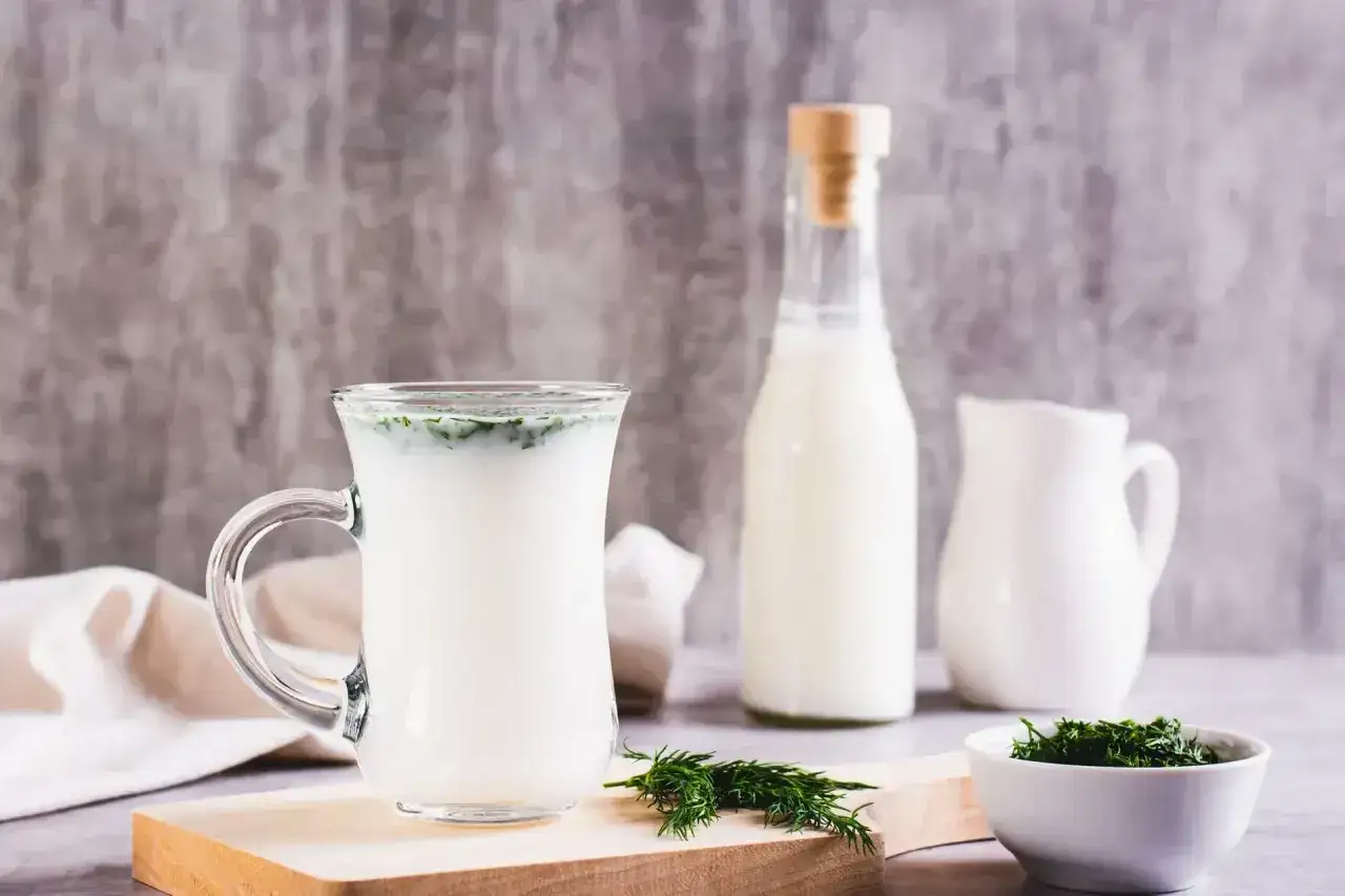 Szklanka z napojem, butelka i dzbanek mleka, miseczka z koperkiem. Czy kefir jest zdrowy? Tak, to pyszny i pożywny napój.