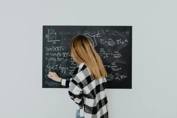 Dziewczyna w kratkę pisze wzór na tablicy. Wzór na t to skomplikowane równanie matematyczne.